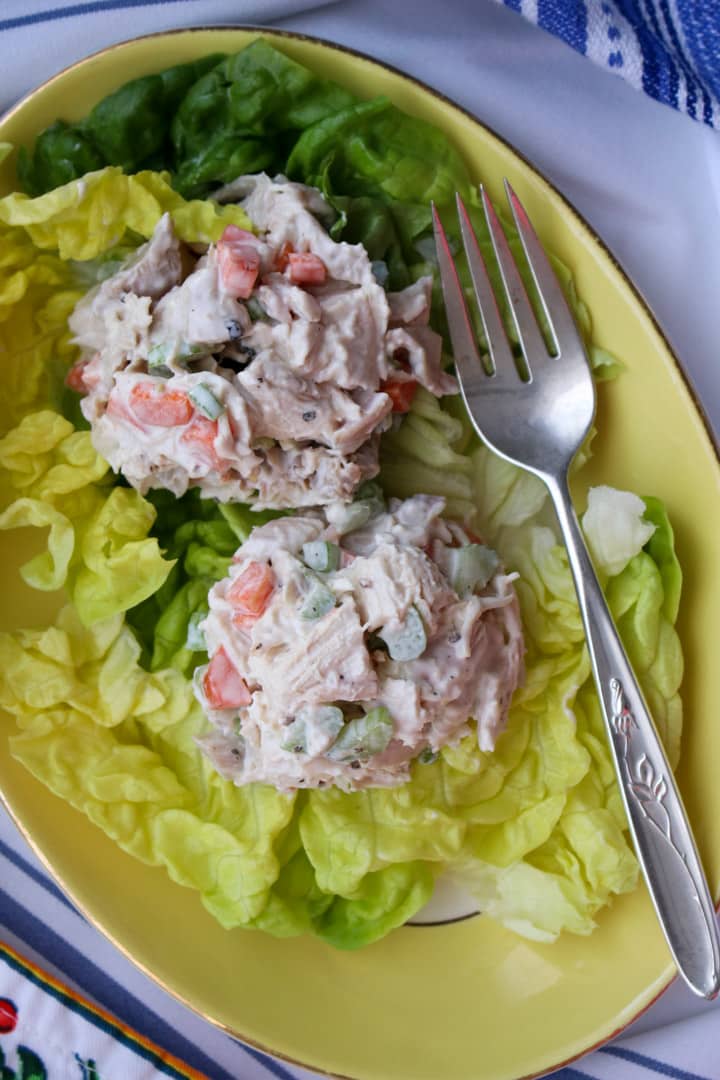 two scoops of chicken salad on lettuce leaves on a yellow plate