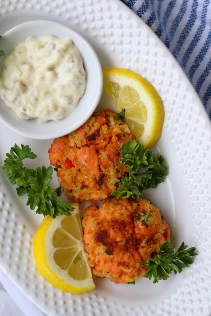 two salmon patties, lemon slices, and tartar sauce on a plate