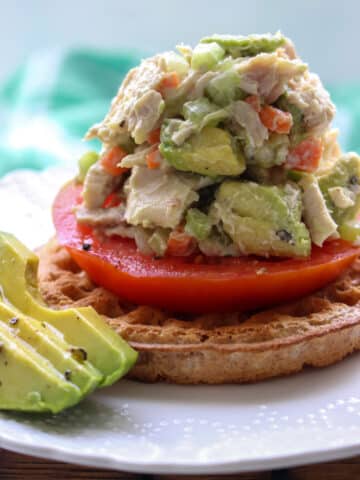 avocado chicken salad on top of a waffle and tomato slice with extra avocado on the side