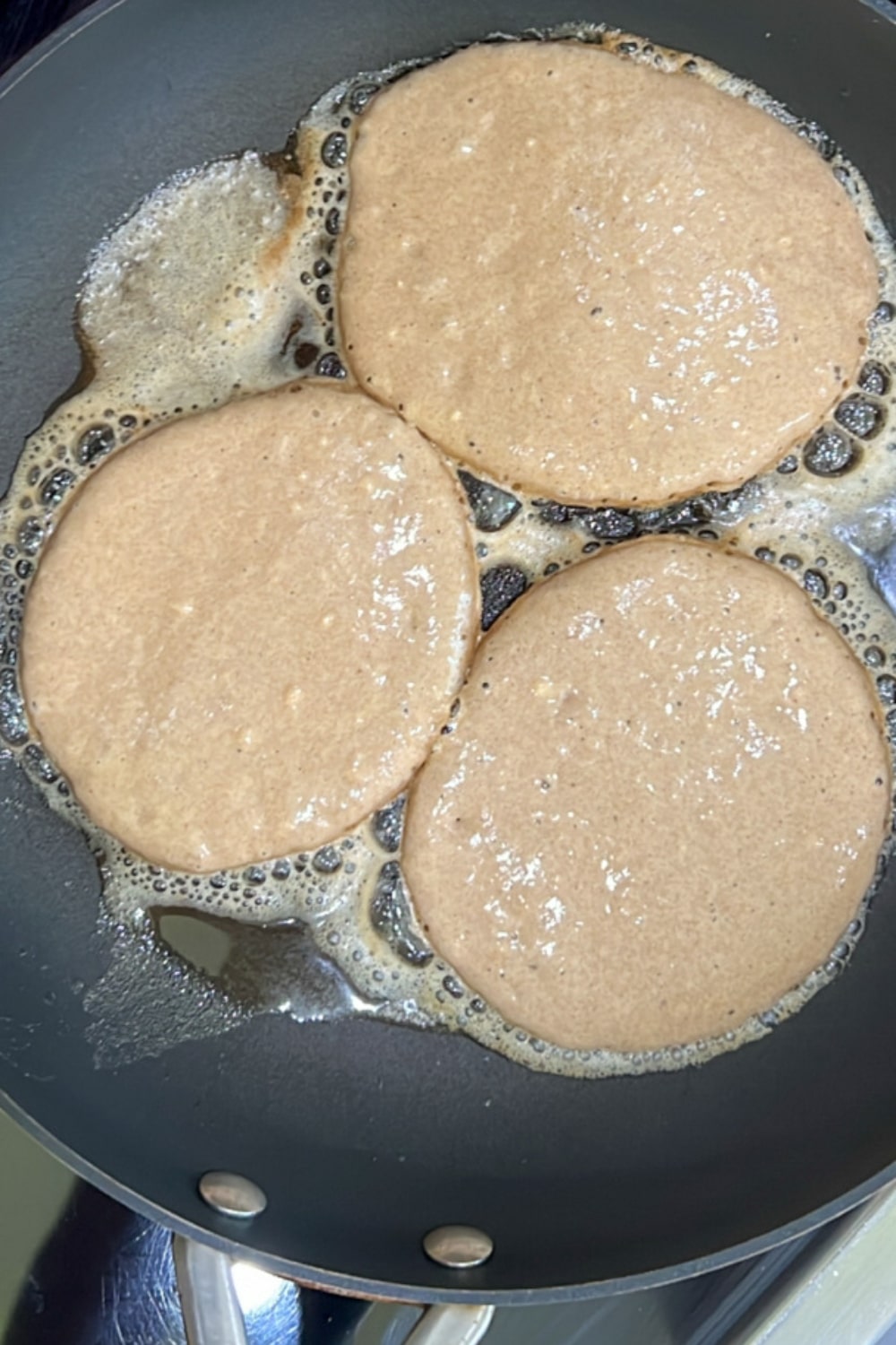 3 pancakes in skillet cooking