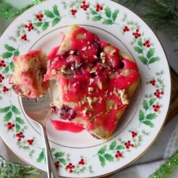 slice of baked cranberry pancake topped with cranberry glaze on a Christmas plate with fork on left side of plate.