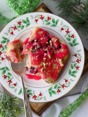 slice of baked cranberry pancake topped with cranberry glaze on a Christmas plate with fork on left side of plate.