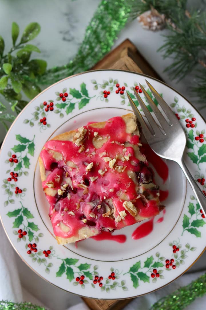 slice of baked cranberry pancake topped with cranberry glaze on a Christmas plate with fork on right side of plate.