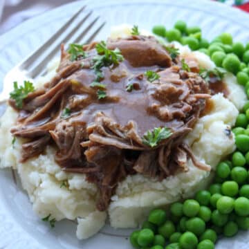 mashed potatoes topped with roast beef, and gravy with peas on the side