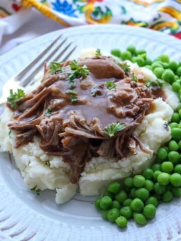 mashed potatoes topped with roast beef, and gravy with peas on the side