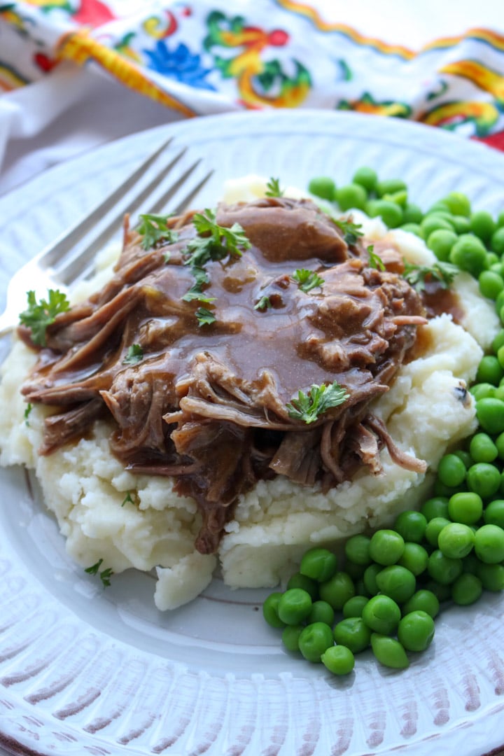 mashed potatoes topped with roast beef, and gravy with peas on the side