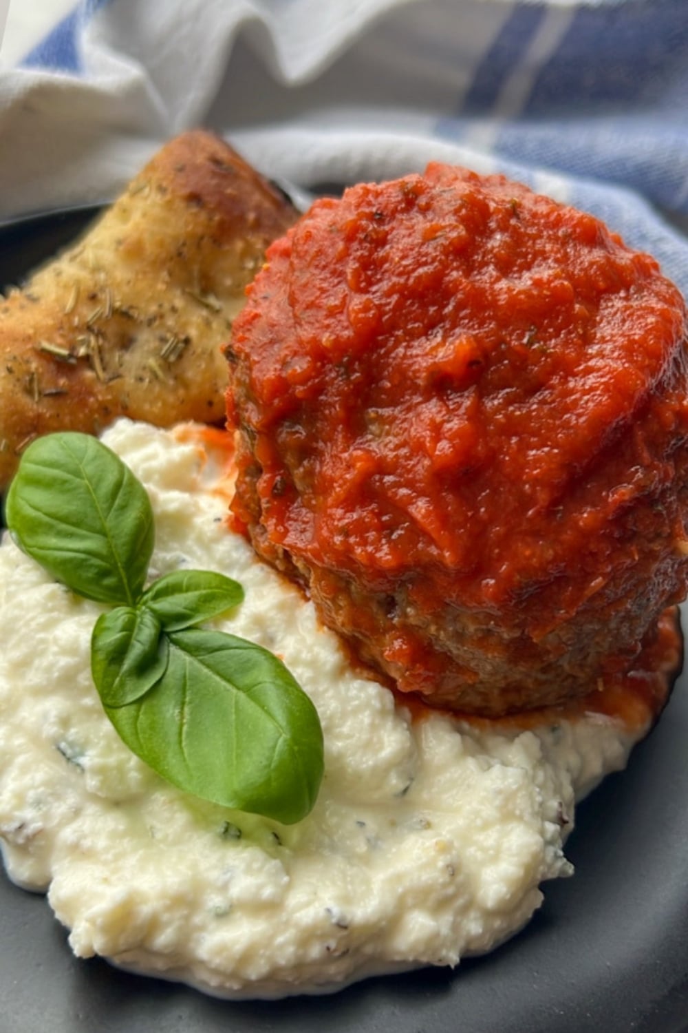 A large meatball on a plate with ricotta and a slice of pizza bread