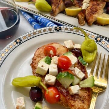GREEK CHICKEN ON A PLATE WITH PLATTER IN BACKGROUND