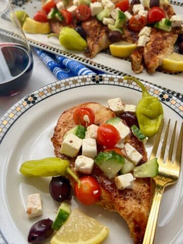 GREEK CHICKEN ON A PLATE WITH PLATTER IN BACKGROUND