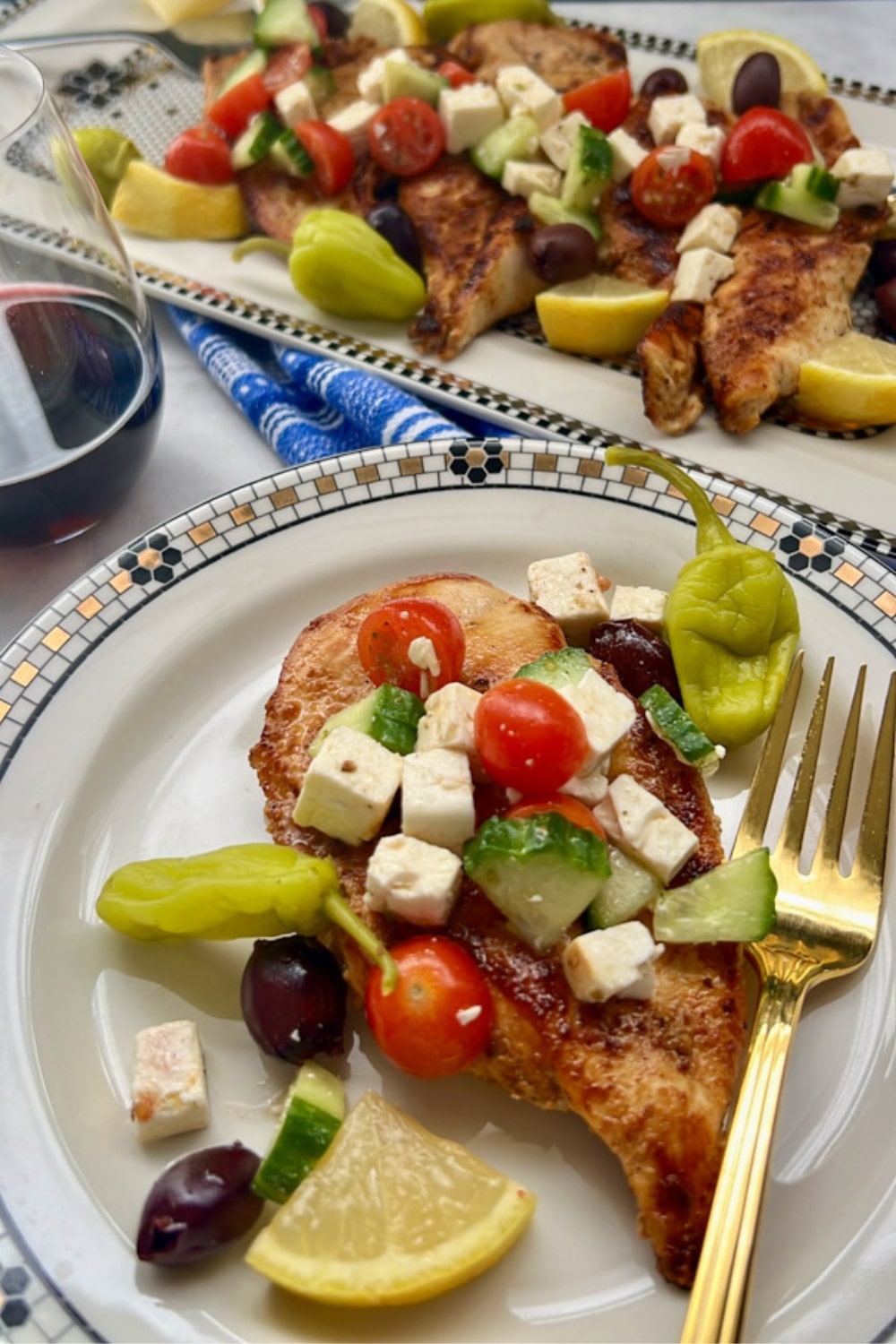 GREEK CHICKEN ON A PLATE WITH PLATTER IN BACKGROUND