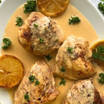 platter of chicken thighs on a parmesan lemon sauce garnished with parsley