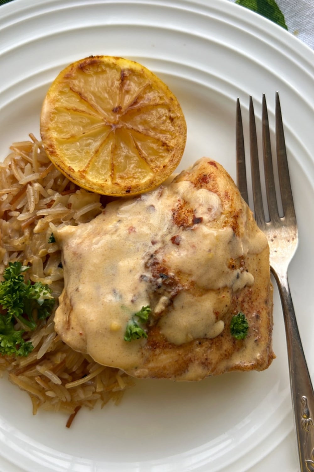 chicken thigh and rice on a plate. Charred lemon on the side.