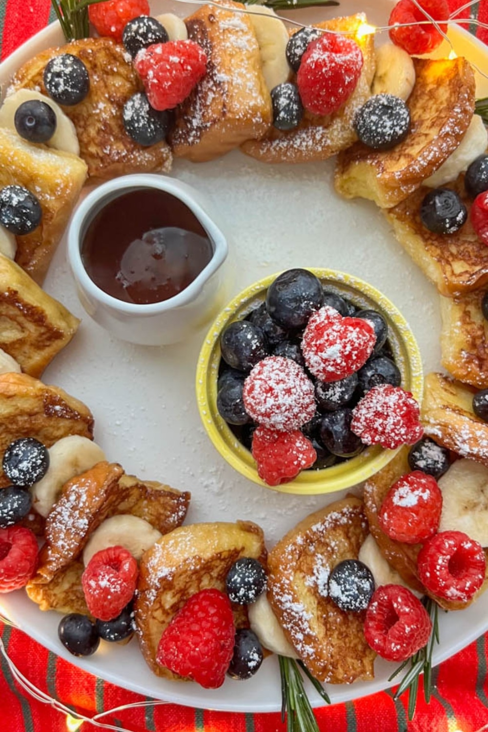 A festive Hawaiian Roll French Toast Wreath with syrup and fresh fruit in the middle.