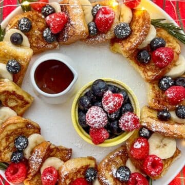 A festive Hawaiian Roll French Toast Wreath with syrup and fresh fruit in the middle.