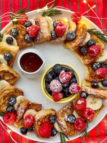 A festive Hawaiian Roll French Toast Wreath with syrup and fresh fruit in the middle.