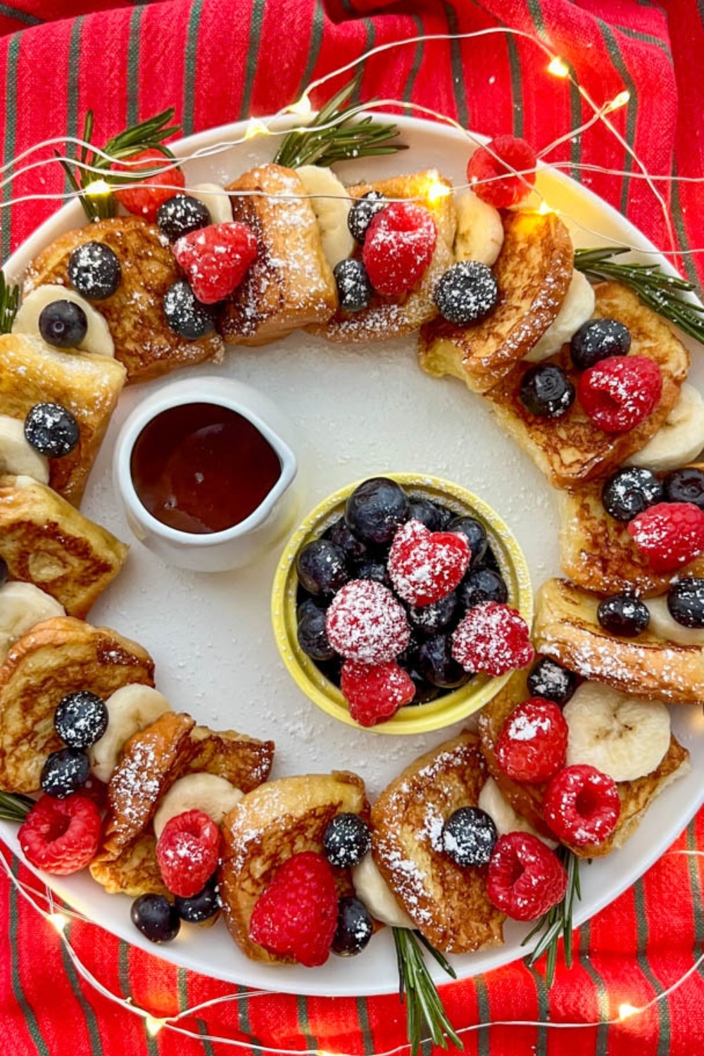 A festive Hawaiian Roll French Toast Wreath with syrup and fresh fruit in the middle.