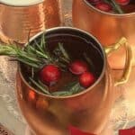 Merry mule cocktail in a mule glass garnished with rosemary and cranberries