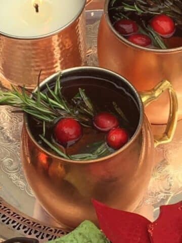 Merry mule cocktail in a mule glass garnished with rosemary and cranberries