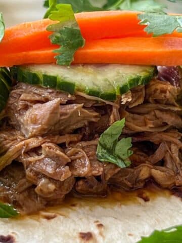 CLOSE UP SLOW COOKER HOISIN PORK SHOULDER COOKED AND TOPPED WITH CUCUMBERS AND CARROTS