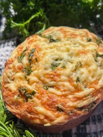 Round loaf of parmesan herb quick bread surrounded by fresh herbs